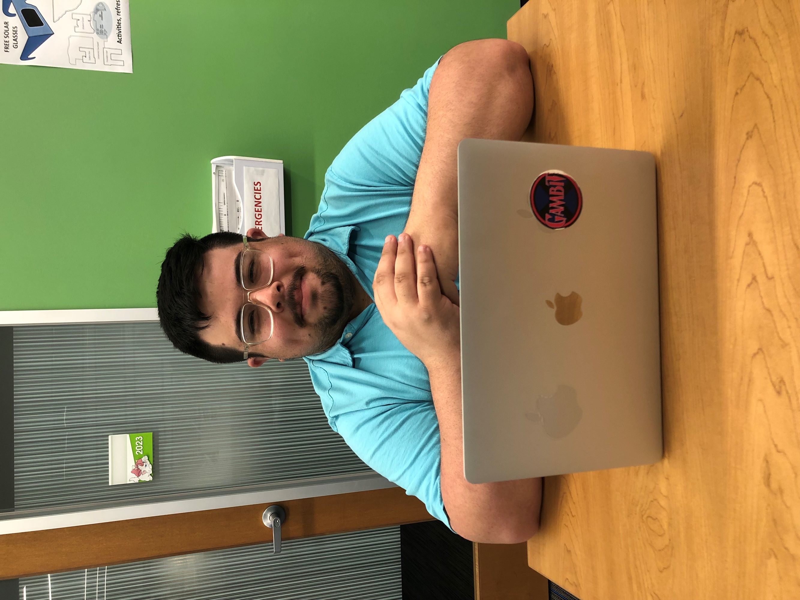 gustavo in glasses and light blue shirt sitting behind a silver laptop smiling