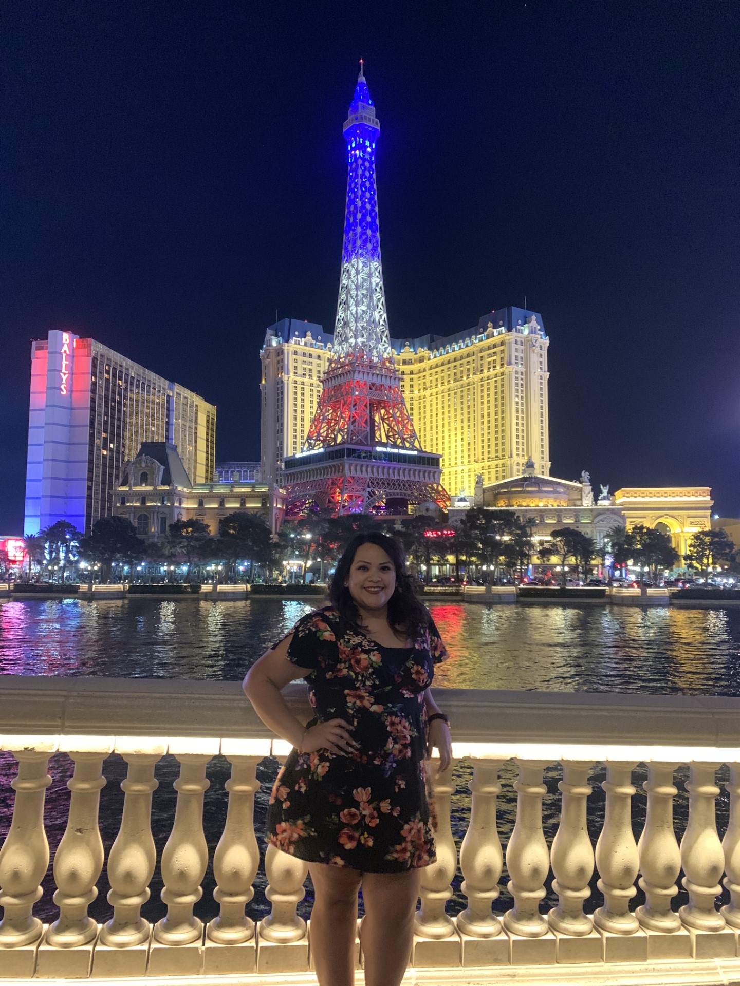 yareli is standing in a dark gloral dress in front of water and a red white and blue eiffel tower